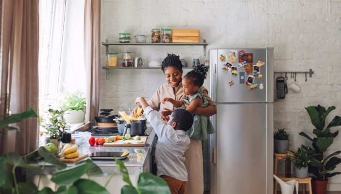 A mother and children cook at a stove; a top freezer fridge is in the background