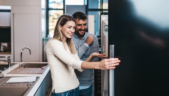 A man and woman open up a black fridge in an appliance showroom