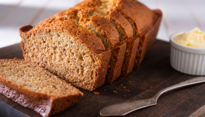 A sliced loaf of banana bread on a wooden board.