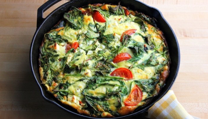 A tomato, spinach egg frittata in a cast iron skillet.