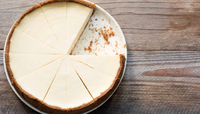 A plain cheesecake with one piece missing on a wooden board.