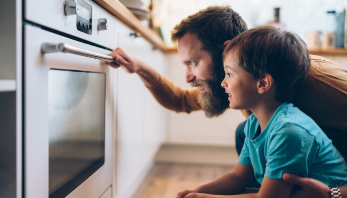 A father and son excitedly look into an oven in their kitchen.
