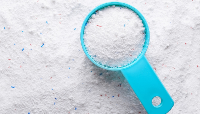 A laundry powder detergent scoop lays full on a table of powdered detergent.
