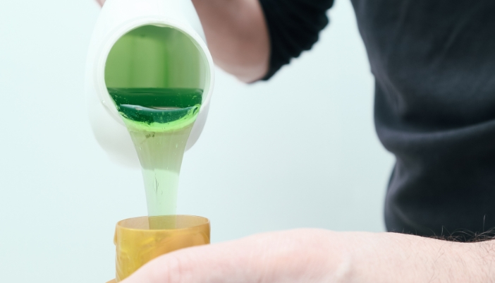A pair of hands pours out green laundry detergent into a cap.