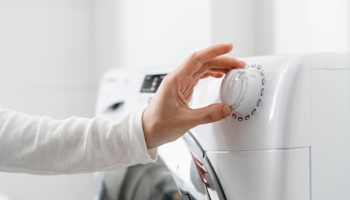 A hand adjusts the dial on a home washing machine.