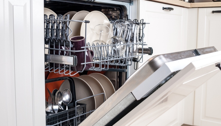 A propped open fully loaded dishwasher in a kitchen with white cabinets.