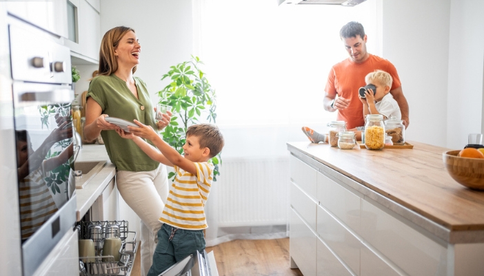 A smiling family unloads a dishwasher in their kitchen together.