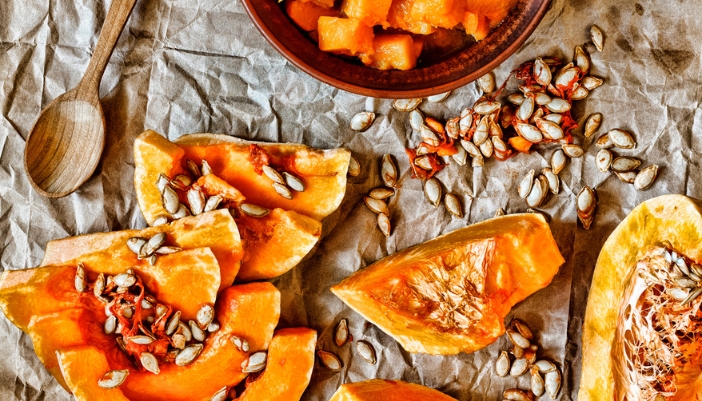 A cut up pumpkin with seeds spilling out on a parchment paper table.