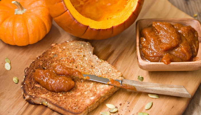 A knife spreads pumpkin seed button on a piece of toast.
