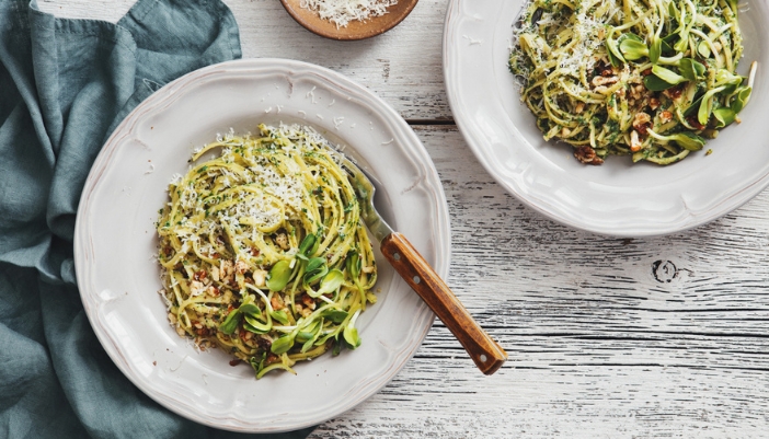  Two bowls of pesto pasta rest on a neutral background.