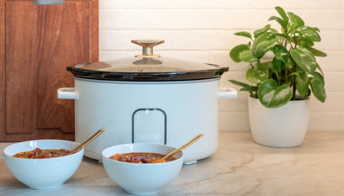 A white slow cooker sits on a countertop with two full bowls in front of it.