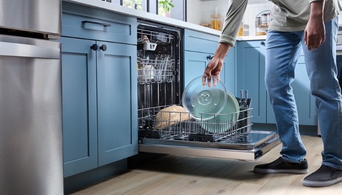 A male loads a dishwasher in a modern kitchen with blue cupboards.