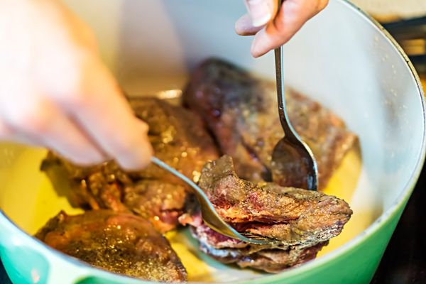 A person searing meat inside of a dutch oven 