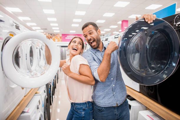 front view of a happy couple smiling and opening washing machines in an appliance store