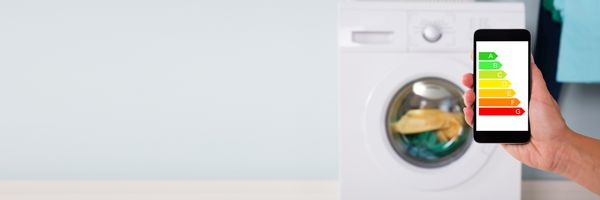 A person holding a smart phone with a graphic letter rating in front of a washer 