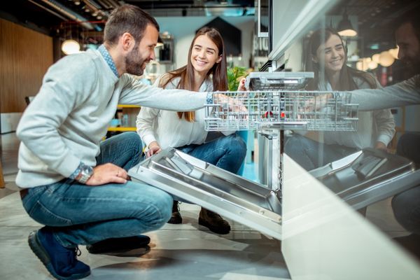 A man and a woman smiling while reviewing a dishwasher 