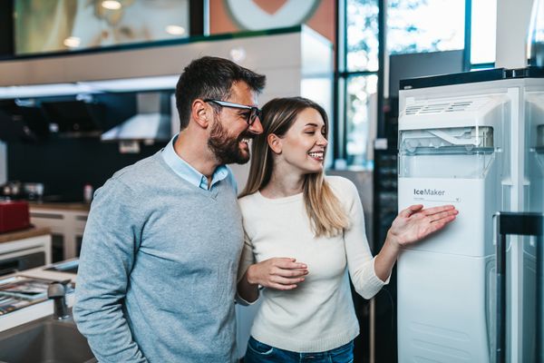 A man and a woman smiling while inspecting the inside of a refrigerator