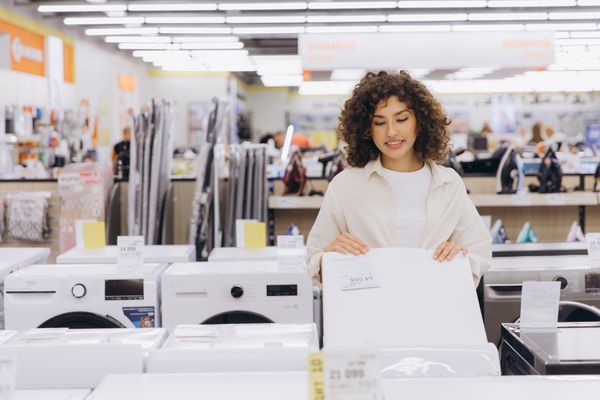 A smiling woman reviewing a top load washing machine a store 