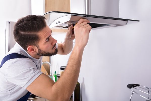 An appliance technician installing a canopy range hood 