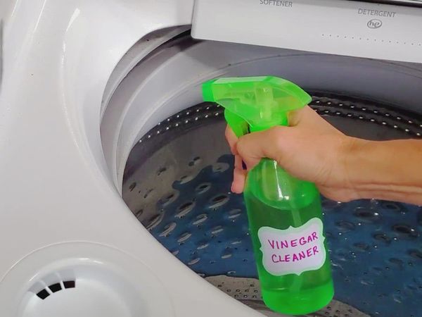 hand with spray bottle of vinegar being held inside a washing machine