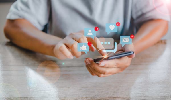 A person using a smart phone with social media graphics projecting from it 