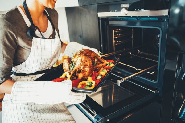 A woman removing a roasted turkey from an oven 