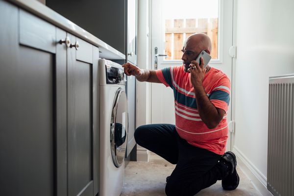 A man on a phone grimacing while operating a front load washer