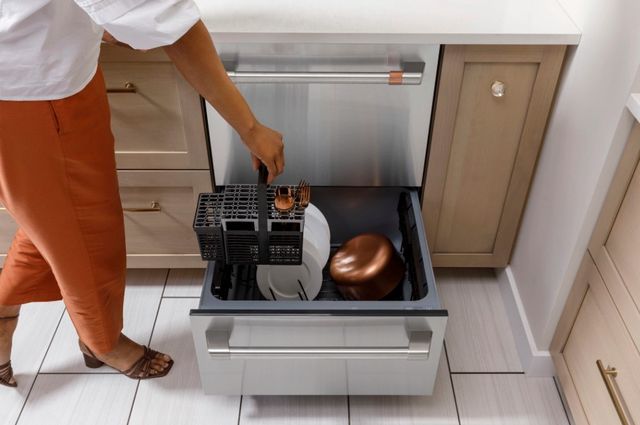 Front view of a woman placing a silverware holder into the bottom drawer of the Cafe double drawer dishwasher