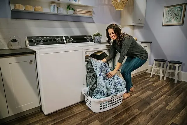 woman loading a blue comforter into a speed queen dryer