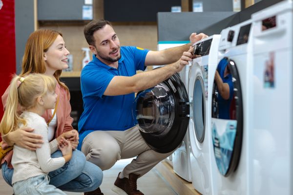 A salesman demonstrating a front load washer to a woman and child 