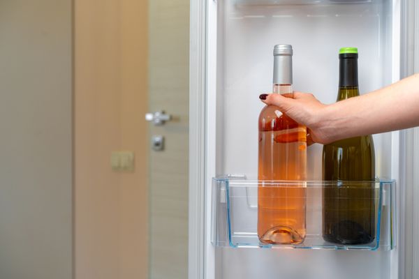 A person grabbing a wine bottle from a fridge bin 