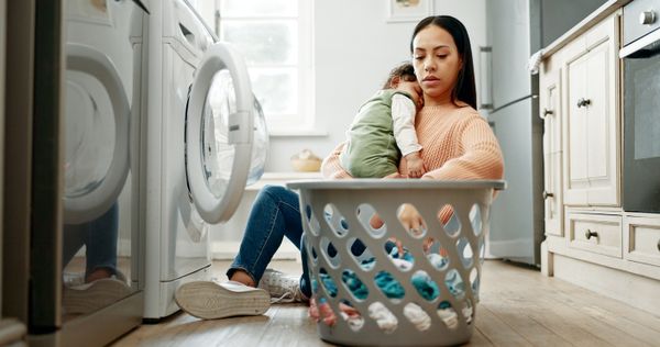 A woman holding a baby loading a washer 