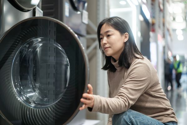 A woman in a tan turtle neck inspecting a front load washing machine 