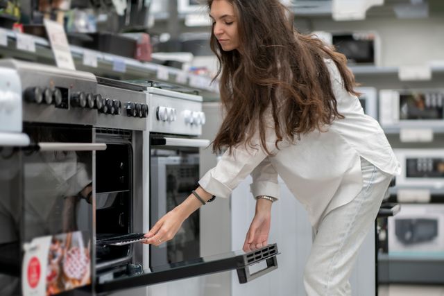 View of a woman dressed in white leading over to examine a range in an appliance store.