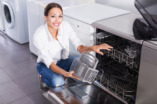 A smiling woman inspecting the inside of a dishwasher 