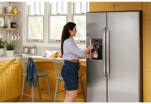 Credit: GE A woman using the ice dispenser on the GE GSS25GYPFS side by side fridge
