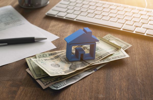 A wooden house figurine on a stack of money 