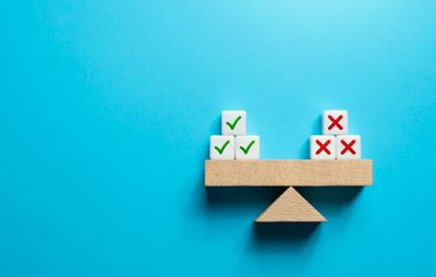 A wooden scale with pros and cons tokens against a blue background 