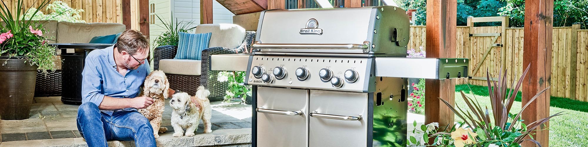 A man and two dogs seated beside a Broil King freestanding grill 
