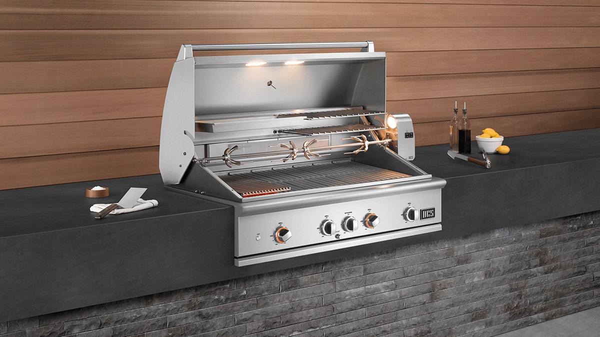 A DCS built-in grill shown opened with a rotisserie spit and halogen lighting 