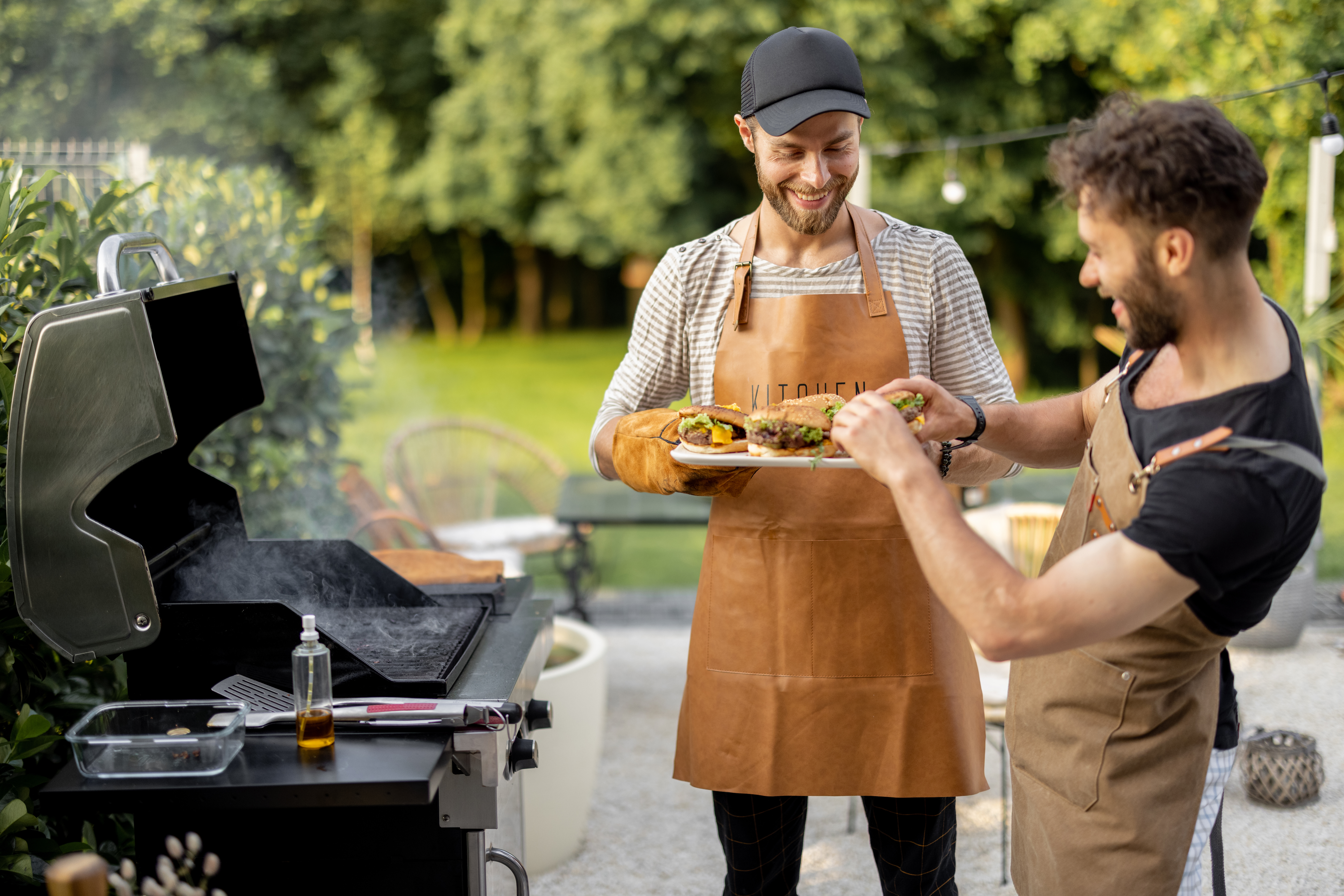 Two men smile while grilling on a freestanding grill 