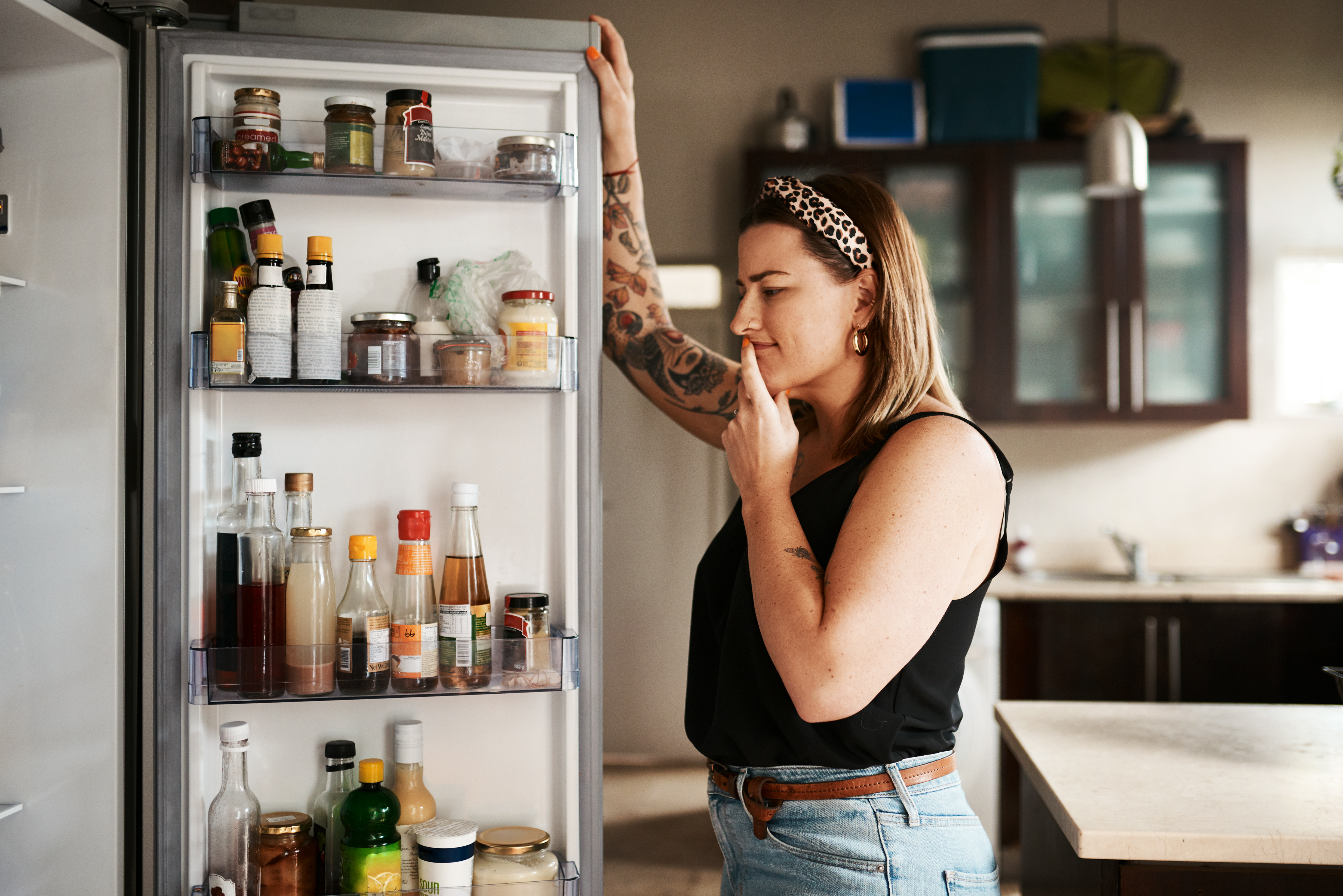 An alternative woman pondering in front of a refrigerator with the door open 