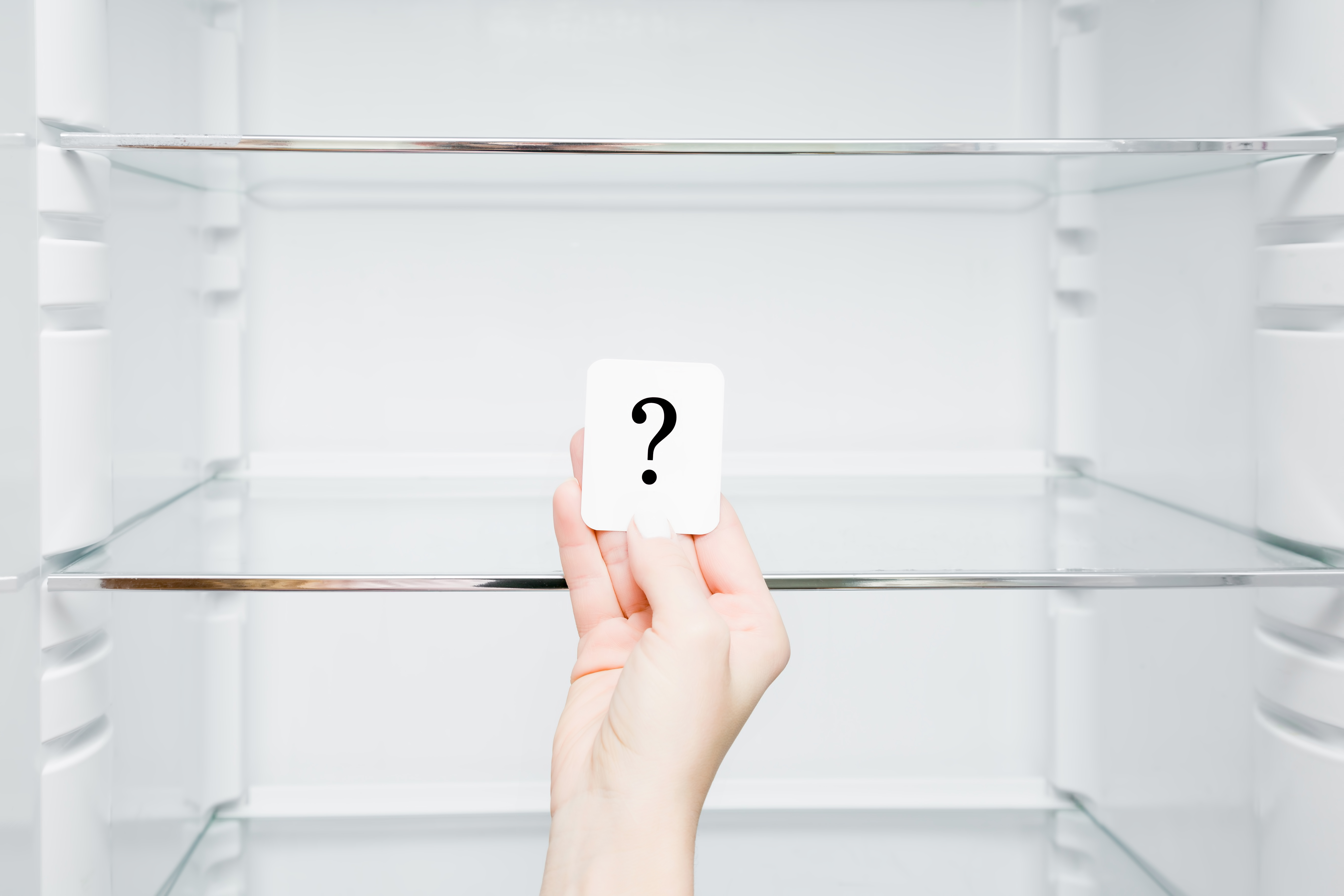 A person holding a paper with a question mark inside of a a refrigerator 