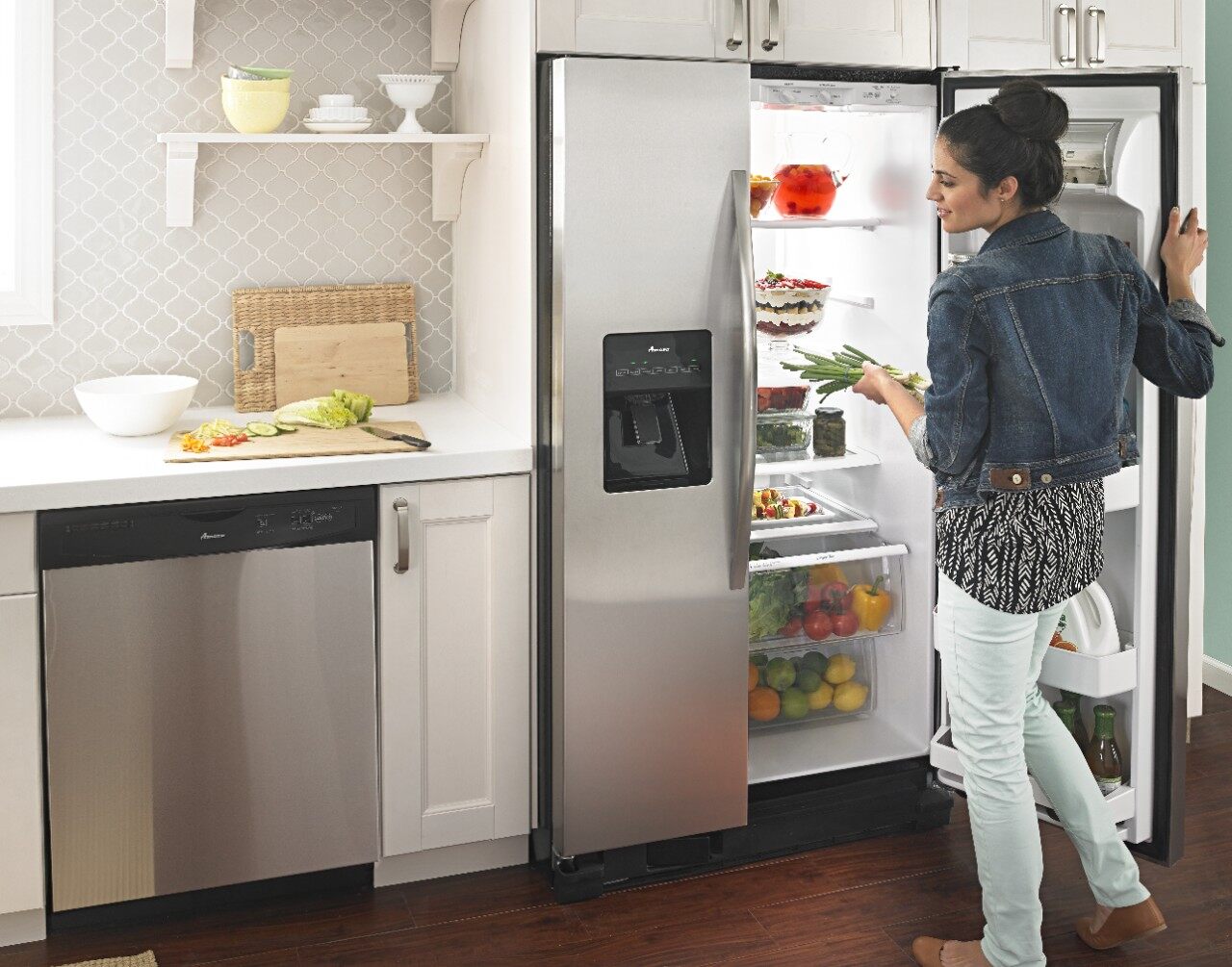 A woman grabbing items from inside an Amana side by side refrigerator 