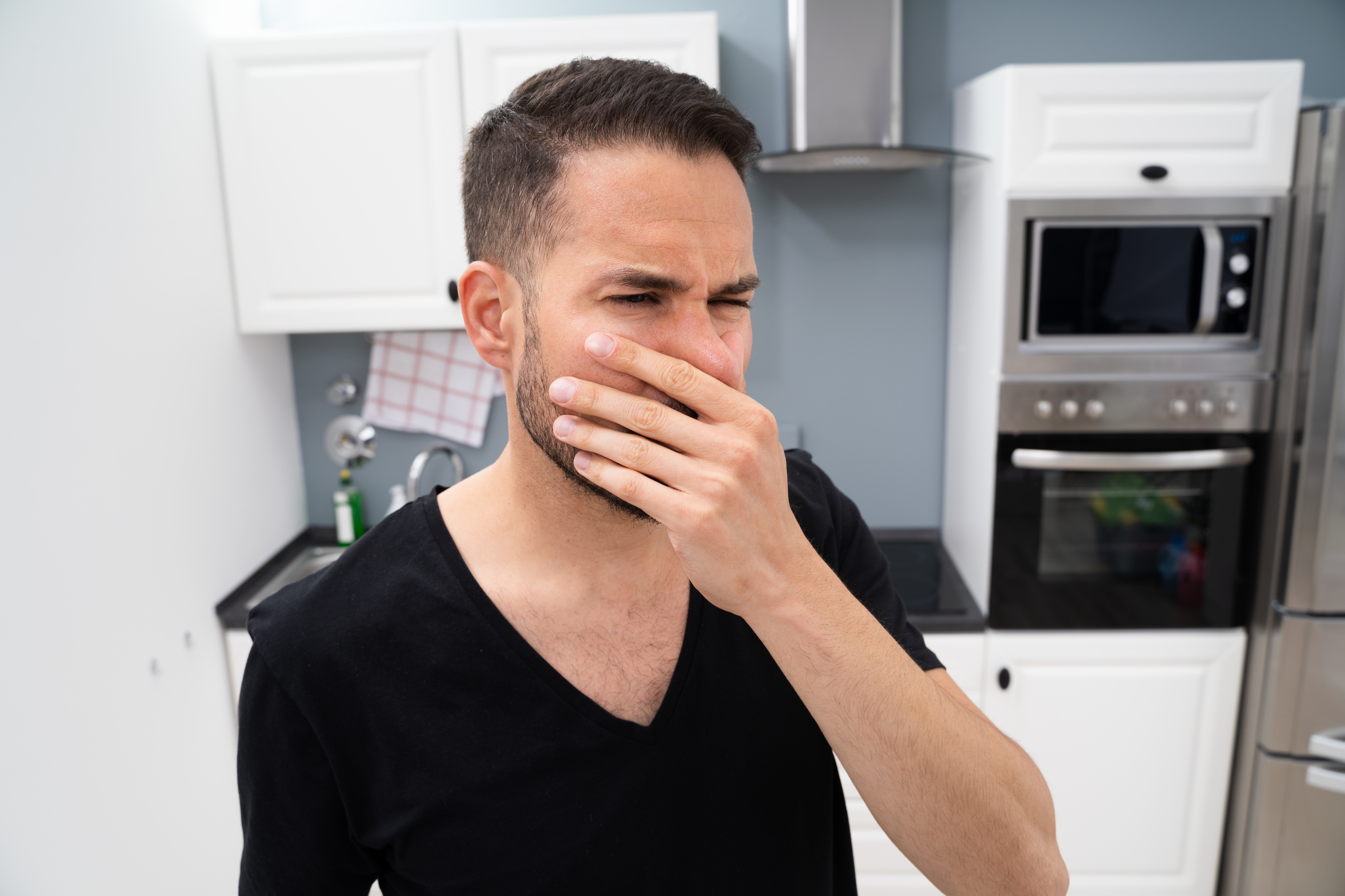 Man in a black shirt covering his nose in disgust in a kitchen 