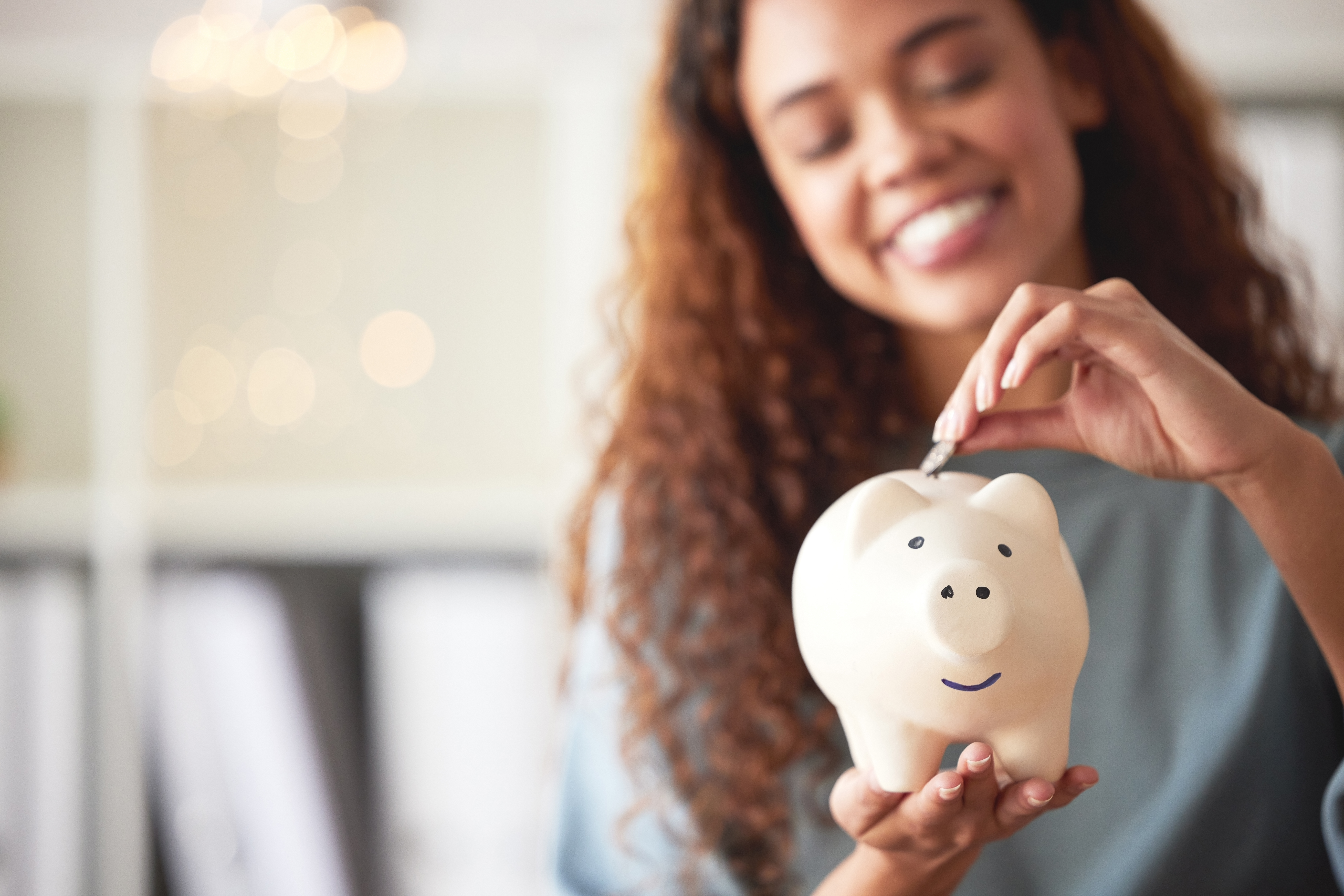 A young woman placing a dollar into a piggy bank 