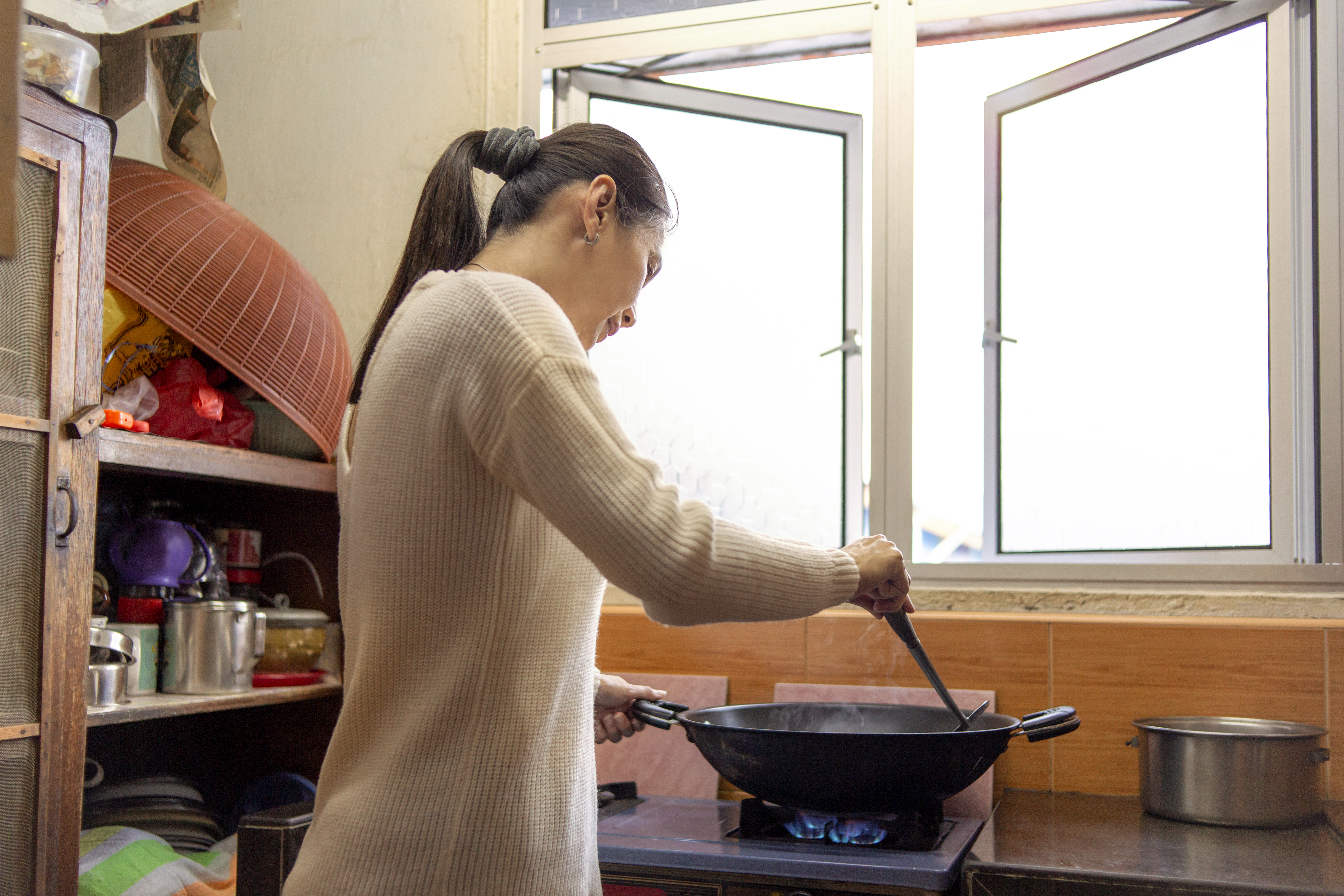 An Asian woman cooking food inside of a wok 