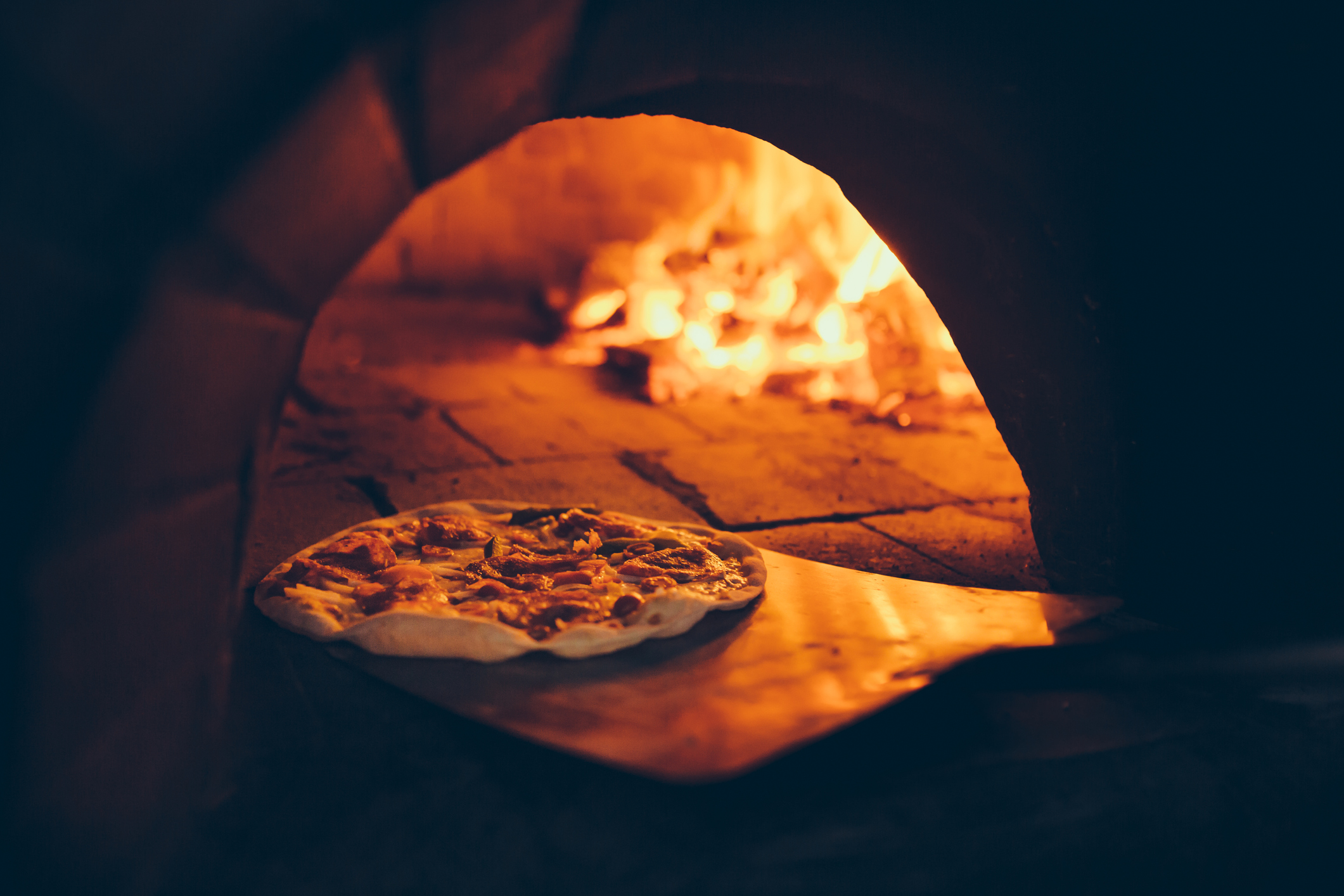 close view of a pizza cooking inside an outdoor pizza oven