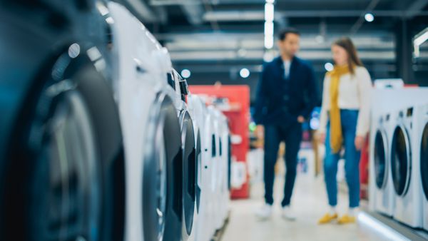 A shot of a blurred couple in the background with a front load washer in the foreground