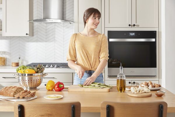 A smiling woman preparing a meal with a Whirlpool oven in the background 